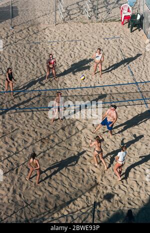 Gruppe von jungen Leuten, die Beachvolleyball spielen, von oben eingerahmt, mit dem niedrigen Licht der Sonne, das lange Schatten zieht Stockfoto