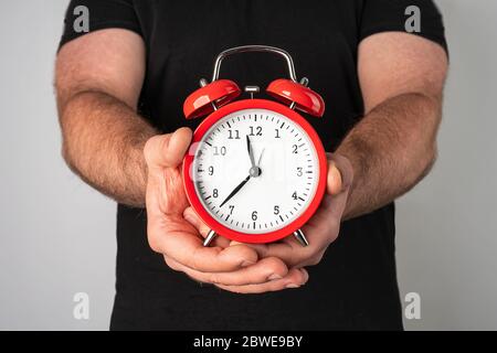 Kaukasischer Mann in schwarzem T-Shirt mit Vintage roten Wecker in seinen Händen Stockfoto