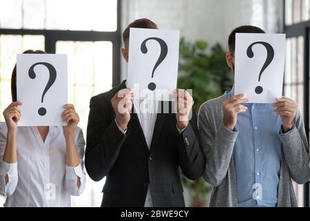 Nahaufnahme von Arbeitern, die Gesichter hinter Papieren mit Fragezeichen verstecken Stockfoto