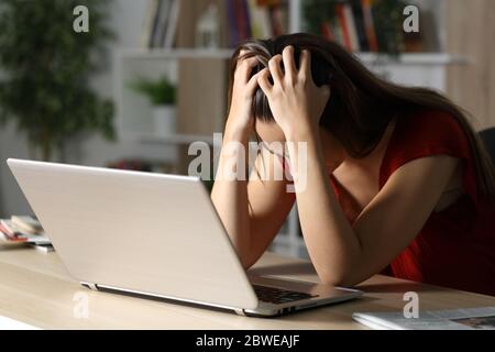Traurige Frau mit Laptop, die sich beschwert, nachts alleine auf dem Schreibtisch zu Hause zu sitzen Stockfoto