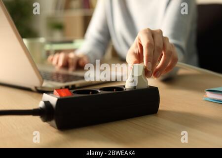 Nahaufnahme einer Frau, die nachts mit einem Laptop auf einem Schreibtisch zu Hause einen Stecker an eine Steckdose steckt Stockfoto