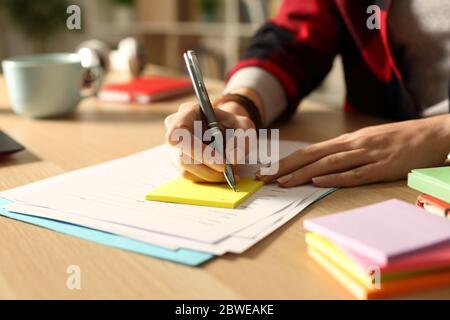 Nahaufnahme von Student Mädchen Hand Schreiben auf Post-Note auf einem Schreibtisch in der Nacht Stockfoto