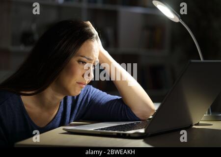 Traurige Frau, die sich über den Laptop beschwert, nachts alleine zu Hause zu sitzen Stockfoto