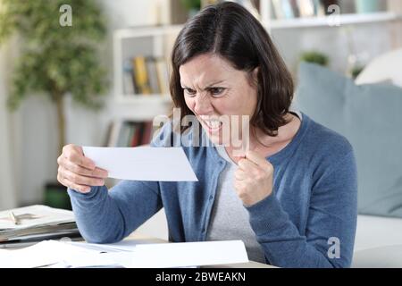 Wütende Erwachsene Frau, die auf Quittungen schaut, die im Wohnzimmer zu Hause sitzen Stockfoto