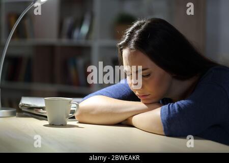 Traurige Frau, die sich nachts im Wohnzimmer zu Hause auf einem Tisch beschwert Stockfoto