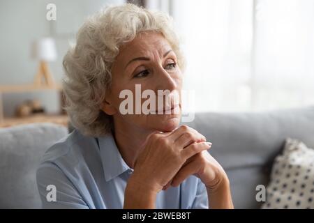 Nachdenkliche ältere Frau auf der Couch, die in nostalgischen Gedanken verloren ist Stockfoto