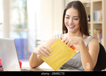 Glückliche Studentin Frau Öffnung gepolsterten Umschlag sitzen auf einem Schreibtisch zu Hause Stockfoto