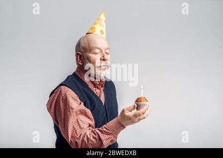 Lächelnder älterer Mann in der Mütze zeigt Kuchen mit Kerze Stockfoto