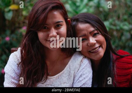 Indonesische Mutter in ihren 50ern und brasilianische Tochter in ihren 20ern lächeln beide in die Kamera. Stockfoto