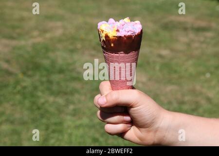 Jungen Hand mit Tesco Rainbow Eiscreme Cone, tagsüber, Sommer, 2020 Stockfoto