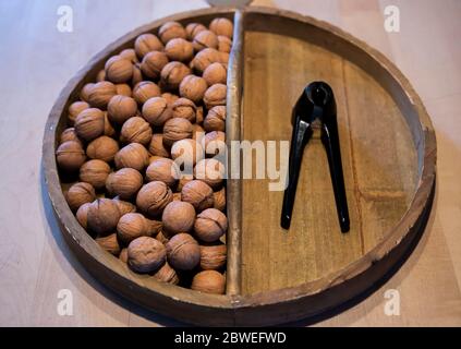 Walnüsse und ein Nussknacker in einer alten runden Holzschale aus einer Sicht von oben gelagert Stockfoto