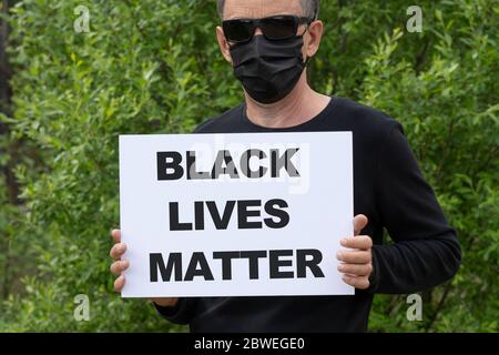 Ein Mann in einer medizinischen schwarzen Maske und schwarzen Brille hält ein weißes Banner mit dem Text SCHWARZ LEBT MATERIE. Stockfoto