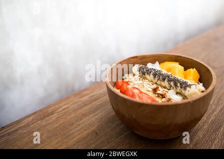 Mango Smoothie Schüssel mit Erdbeere, Banane, Kokosnuss und Haferflocken auf Holzhintergrund. Gesundes Essen Konzept. Stockfoto