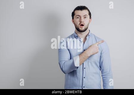 Erfolgreicher Mann zeigt mit dem Finger zur Seite und ist überrascht Stockfoto