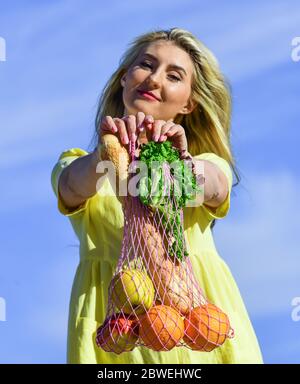 Wiederverwendbare Öko-Tasche zum Einkaufen. Frau hält String Einkaufstasche mit Früchten und Brot auf Himmel Hintergrund. Zero Waste Konzept. Mädchen im Kleid mit String Tasche Shopper. Tasche mit Lebensmitteln. Rohkost Ernährung. Stockfoto