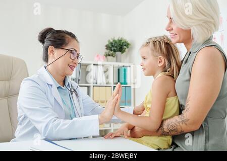 Lächelnd reifen Kinderarzt geben hohe fünf bis wenig Patienten nach ihrer Genesung Stockfoto