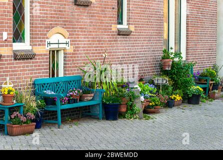 Fassade eines alten holländischen Hauses mit verschiedenen Pflanzgefäßen und Holzbänken auf der Straße mit verschiedenen Blumentöpfen gefüllt mit Blumen auf sie gestellt Stockfoto