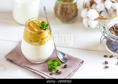 Ein Glas Iced Dalgona Kaffee, trendy flauschigen cremigen Schlagkaffee, von Minze dekoriert. Weiße Holztischfläche mit pinker Serviette. Stockfoto