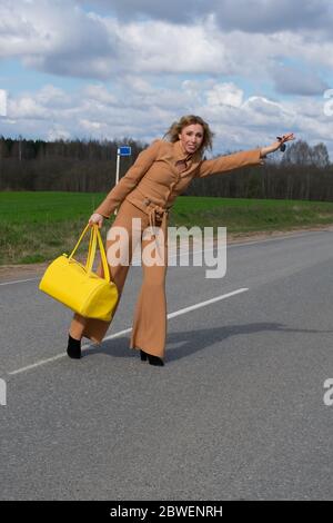 Elegante Frau mittleren Alters in einem modischen Hosenanzug und mit einer gelben Reisetasche in der Hand überquert die Straße. Das Konzept der Erholung von der Stadt und Stockfoto