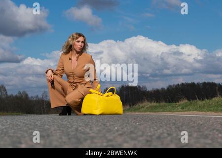 Elegante Frau mittleren Alters in einem modischen Pantait und mit einer gelben Reisetasche in der Hand auf einer leeren Spur. Das Konzept der Ruhe aus dem Stadtleben und tra Stockfoto