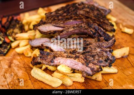 Geschnittenes saftiges vom Grill mariniertes Rindfleisch Flank Steak auf Holzbrett. Saftige medium Fleisch geschnitten und fertig zum Servieren mit Gemüse und gebackene Pota Stockfoto