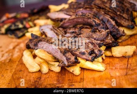 Geschnittenes saftiges vom Grill mariniertes Rindfleisch Flank Steak auf Holzbrett. Saftige medium Fleisch geschnitten und fertig zum Servieren mit Gemüse und gebackene Pota Stockfoto