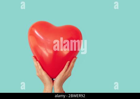 Frau hält roten Herz förmigen Ballon zu einem türkisfarbenen Wand Hintergrund. Valentinstag und Romantik Konzept Stockfoto