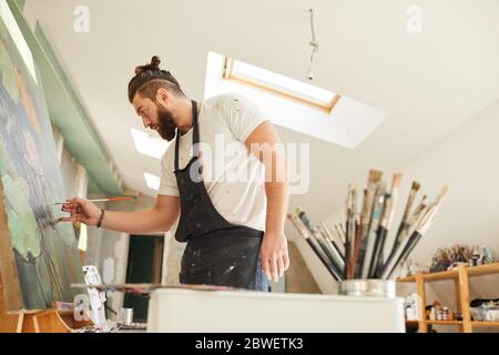 Seitenansicht Porträt von zeitgenössischen bärtigen Künstler Malerei Bild auf Staffelei mit großem Fokus und Aufmerksamkeit während im geräumigen Dachboden Kunststudio stehen Stockfoto