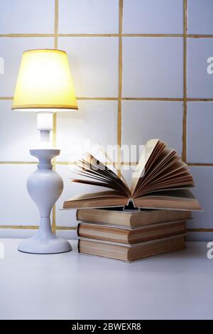 Elegante weiße Schreibtischlampe mit gelbem Lampenschirm in der Nähe des offenen Buches Stockfoto