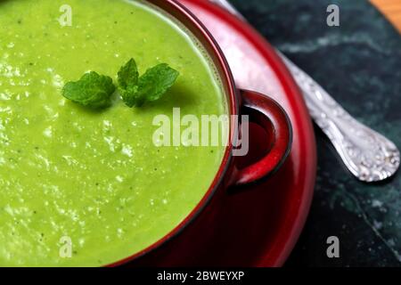 Von oben Schale mit köstlichen hausgemachten pflanzlichen veganen Erbsensuppe mit Blättern aus frischer Minze auf dem Tisch serviert Stockfoto