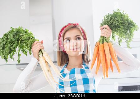 Schönes Mädchen hält Bündel von frischen Karotten und Petersilie in der Küche. Stockfoto