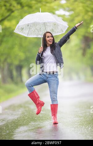 Hübsches Mädchen zeigt sich im Regen mit einem Vintage-Regenschirm, trägt roten Polka Punkt regen Stiefel. Stockfoto