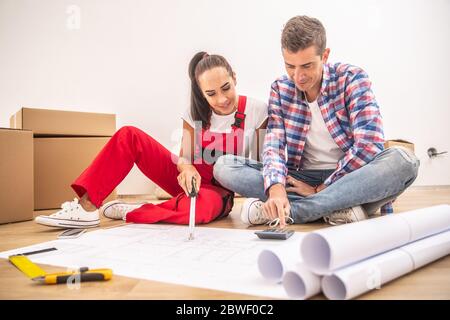 Junges Paar in lässiger Kleidung und einem Gesamtplan die Wohnungsdekoration über Papierpläne. Stockfoto