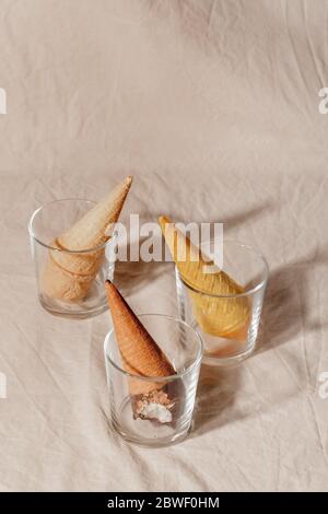 Verschiedene Eis Waffelkegel in Glas auf beigefarbenem Pastellgrund. Kreatives Sommerkonzept Stockfoto