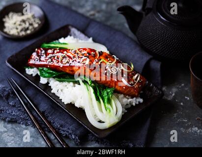 Teriyaki marinierte asiatische Lachsfilet mit Frühlingszwiebeln und Sesamsamen auf einem Bett aus Pak Choi und Jasminreis Stockfoto