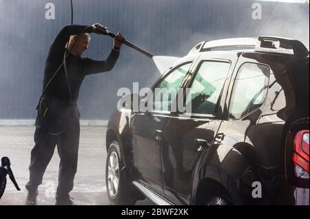 Ein Mann wäscht ein Auto bei einer berührungslosen Autowäsche, ein Mann wäscht ein braunes Auto, Kaliningrad, Russland, 1. März 2020 Stockfoto