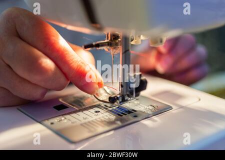 Ältere Frau Finger Einführen eines roten Fadens in eine Nähmaschine Nadel, Nahaufnahme Stockfoto