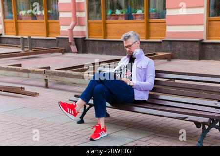 Unbekannter Mann in einer Mundmaske gegen Smog Luftverschmutzung mit PM2.5 sitzt auf einer Bank und liest ein Buch, zu Fuß auf einem Zeitplan. Moskau, Russland, Mai 20 Stockfoto