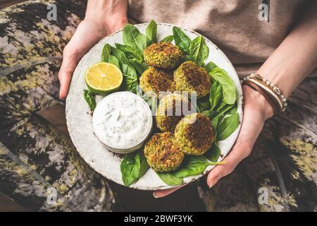 Mädchen hält Teller vegetarische Falafel mit Sauce auf Teller. Gesundes vegetarisches Essen Spinat-Frikadierfutter aus Chickpea mit Joghurtsauce Stockfoto