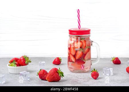 Wasser, Cocktail, Limonade oder Tee mit Erdbeeren. Sommer eisgekühltes Getränk mit Erdbeere, Minzblatt, Eiswürfel auf weißem Holzgrund flach Stockfoto