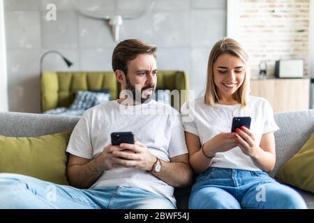 Junges Paar mit Smartphones zu Hause. Eifersüchtiger Freund spioniert das Telefon seiner Freundin. Stockfoto