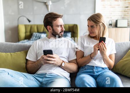 Junges Paar mit Smartphones zu Hause. Eifersüchtiger Freund spioniert das Telefon seiner Freundin. Stockfoto