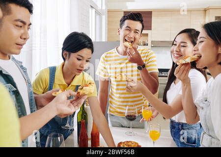 Gruppe von glücklichen jungen asiatischen Menschen genießen köstliche Pizza bei House Party Stockfoto
