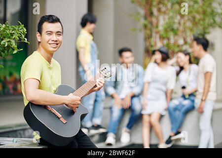Schöner junger asiatischer Student Gitarre im Hinterhof seiner Universität Stockfoto