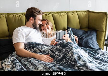 Schöne junge Paar in Liebe zu Hause, im Bett, über Mobiltelefone Stockfoto