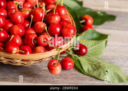 Korb mit süßen und reifen Kirschen mit Blättern auf Holzhintergrund Stockfoto