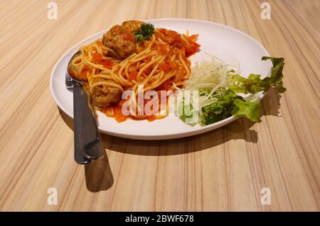 Spaghetti Pasta mit Fleischbällchen und rote Tomatensauce auf Holztisch, italienische Küche auf weißem Teller und Löffel und Gabel Stockfoto