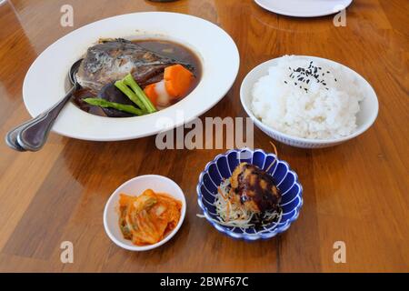 Lachs Kopf in Soja-Quellsuppe mit Zutat in einem weißen Behälter gedämpft, japanische Lebensmittel mit gedämpftem Reis und Kimchee auf braunem Tisch Stockfoto