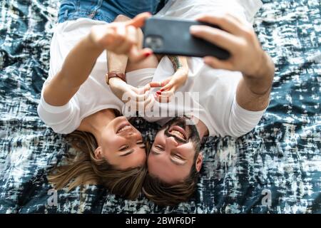 Draufsicht auf schöne junge liebevolle Paar im Bett liegen und Selfie machen Stockfoto