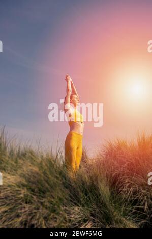 Frau, die in den Dünen steht, praktiziert Yoga und meditiert in der Natur. Stockfoto